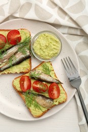 Photo of Delicious sandwiches with sprats, tomatoes, dill and avocado puree served on white wooden table, top view