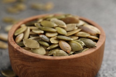 Photo of Wooden bowl with peeled pumpkin seeds on table, closeup