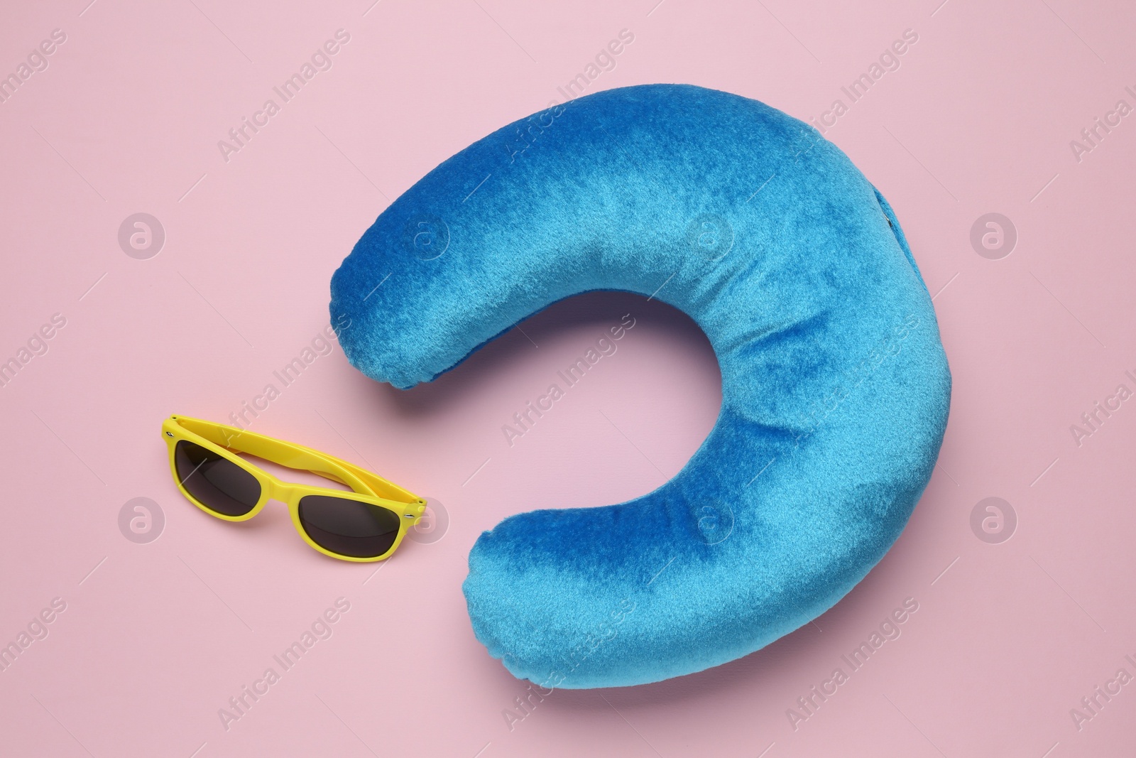 Photo of Light blue travel pillow and sunglasses on pink background, flat lay