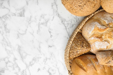 Loaves of different breads on white marble background, flat lay. Space for text