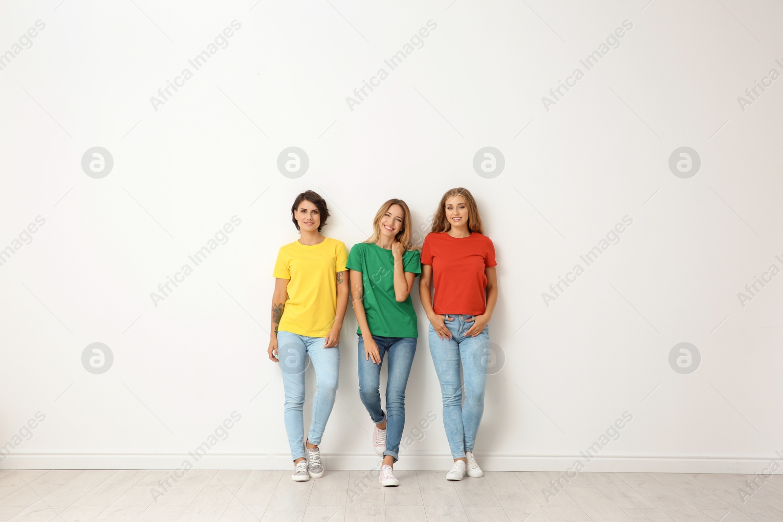 Photo of Group of young women in jeans and colorful t-shirts near light wall