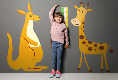 Little girl measuring height and drawings of animals near grey wall