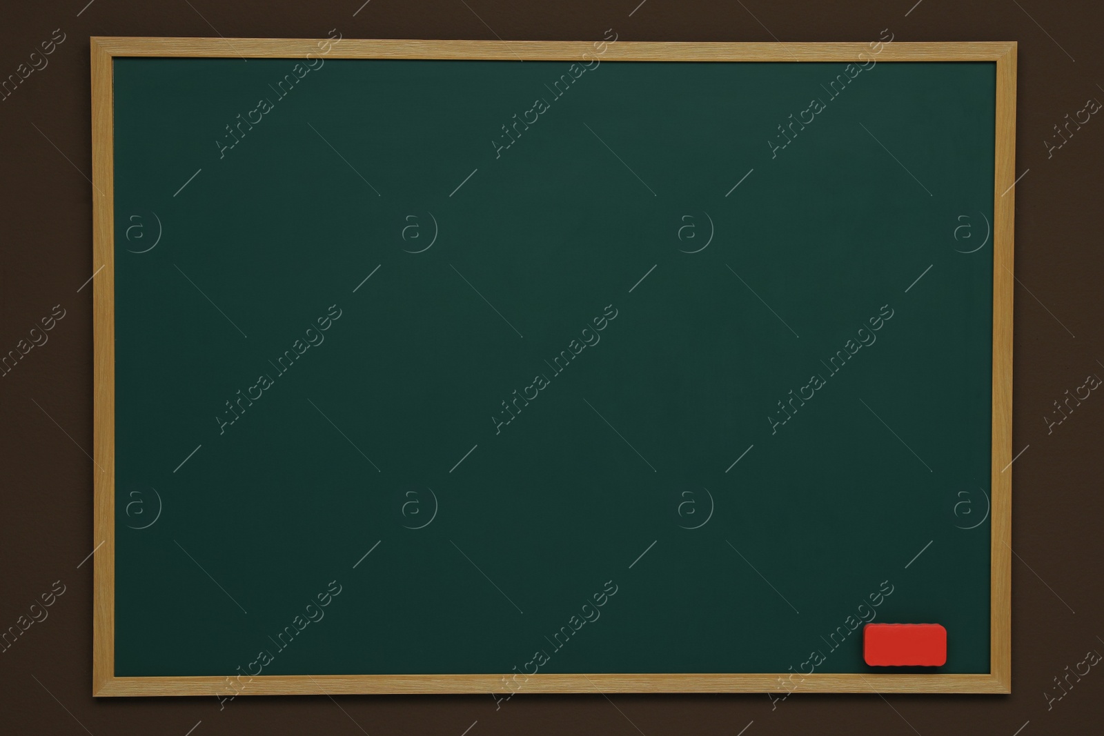 Photo of Clean green chalkboard with duster hanging on brown wall