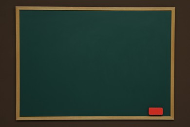 Photo of Clean green chalkboard with duster hanging on brown wall
