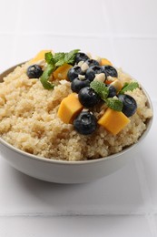 Photo of Tasty quinoa porridge with blueberries, pumpkin and mint in bowl on white table