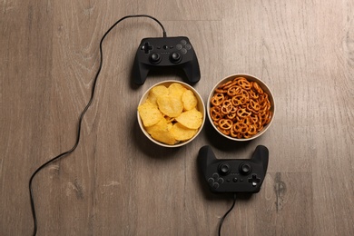 Photo of Flat lay composition with video game controllers and food on wooden background