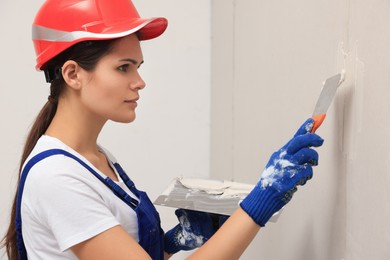 Professional worker in hard hat plastering wall with putty knives indoors