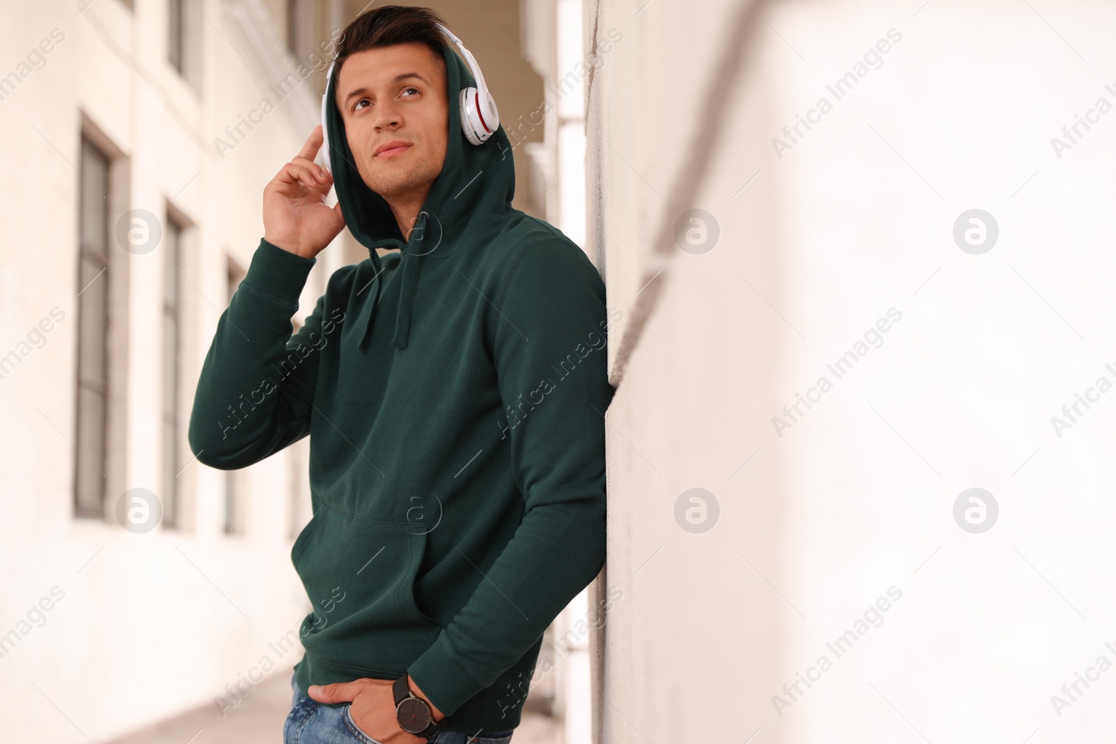 Photo of Portrait of handsome young man with headphones listening to music near stone wall outdoors. Space for text