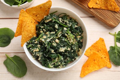 Photo of Tasty spinach dip with eggs in bowl and nachos chips on light wooden table, top view