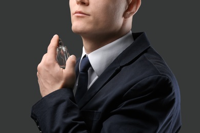 Photo of Handsome man in suit using perfume on dark background, closeup