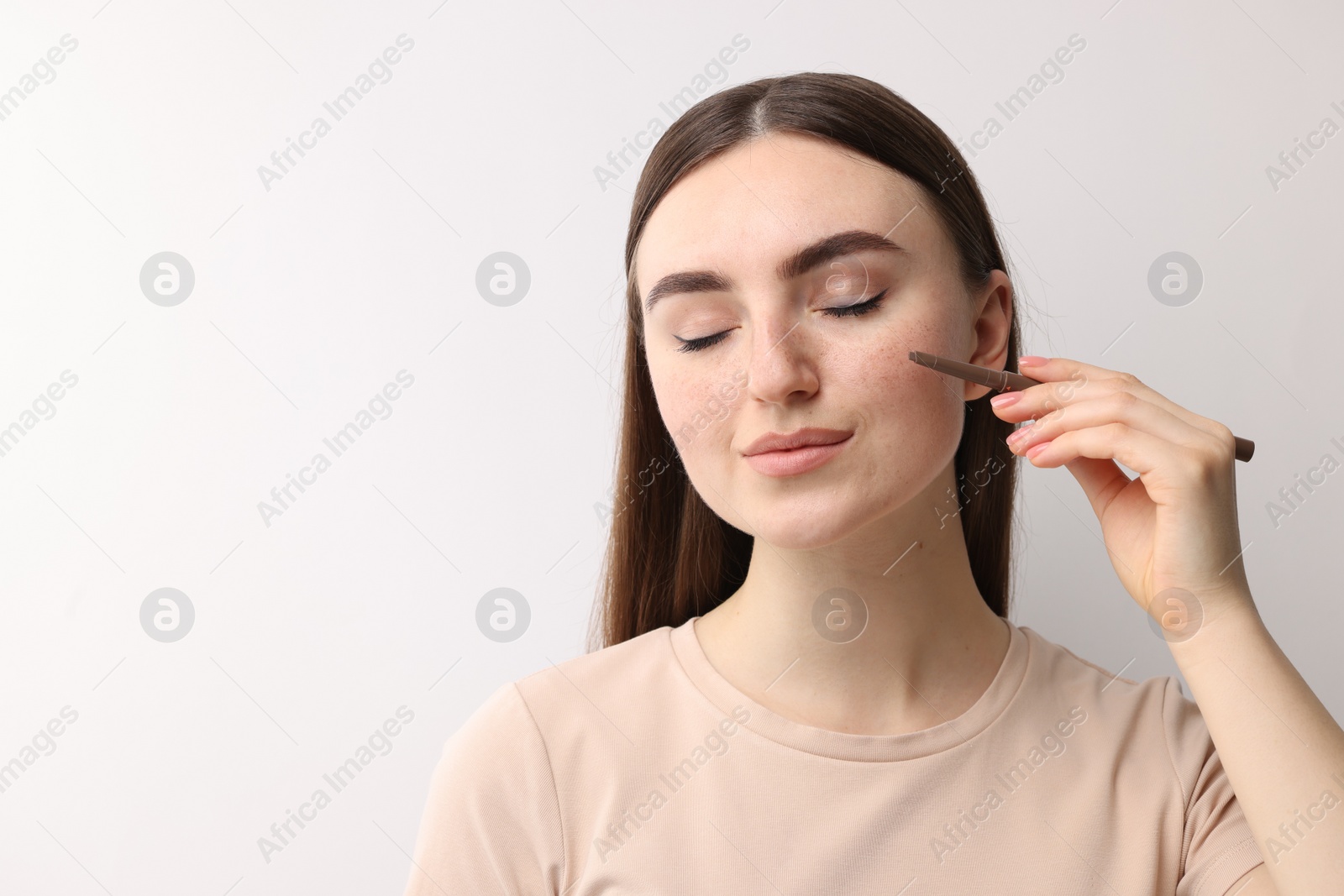 Photo of Beautiful woman drawing freckles with pen on light background. Space for text