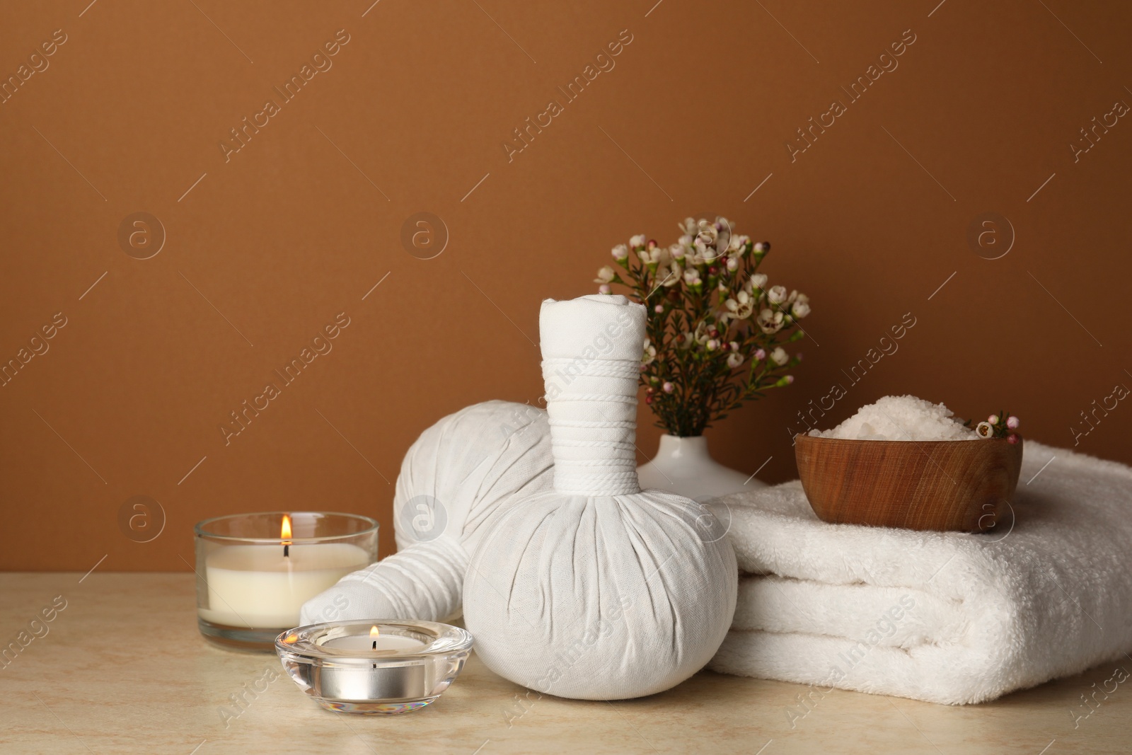 Photo of Composition with different spa products, candles and flowers on beige table against brown background. Space for text