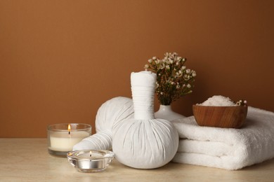 Photo of Composition with different spa products, candles and flowers on beige table against brown background. Space for text