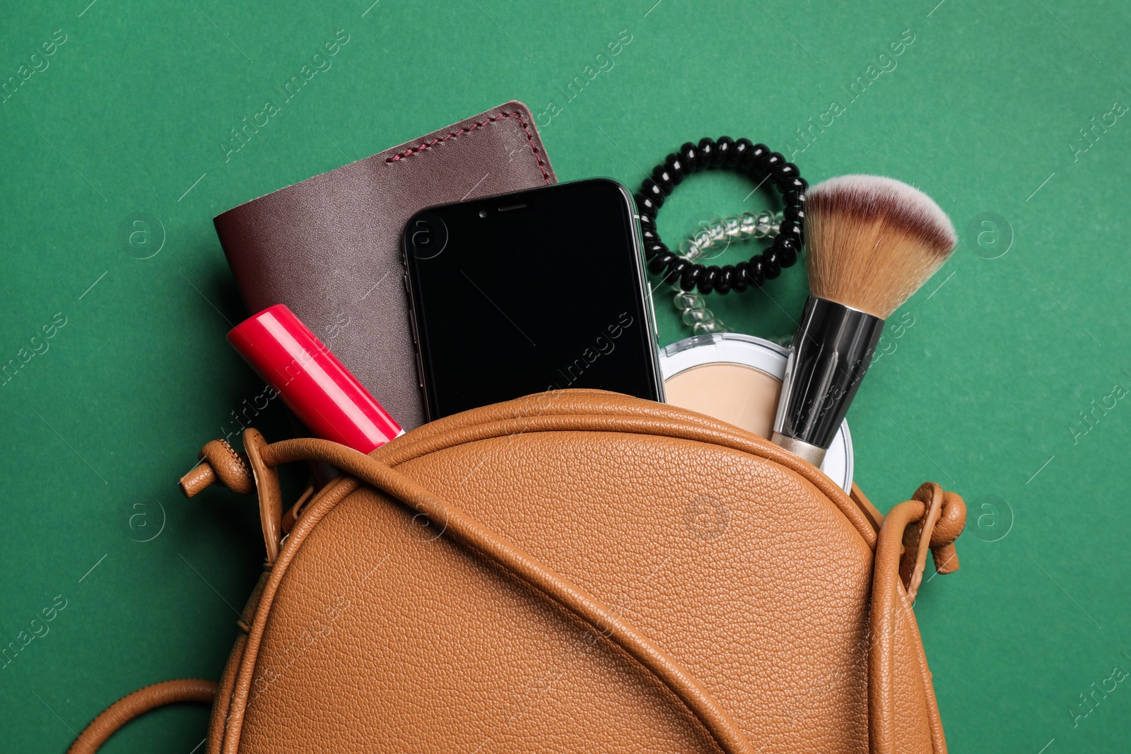 Photo of Stylish woman's bag with smartphone and accessories on green background, flat lay