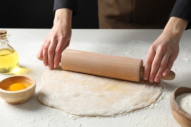 Woman rolling raw dough at table, closeup