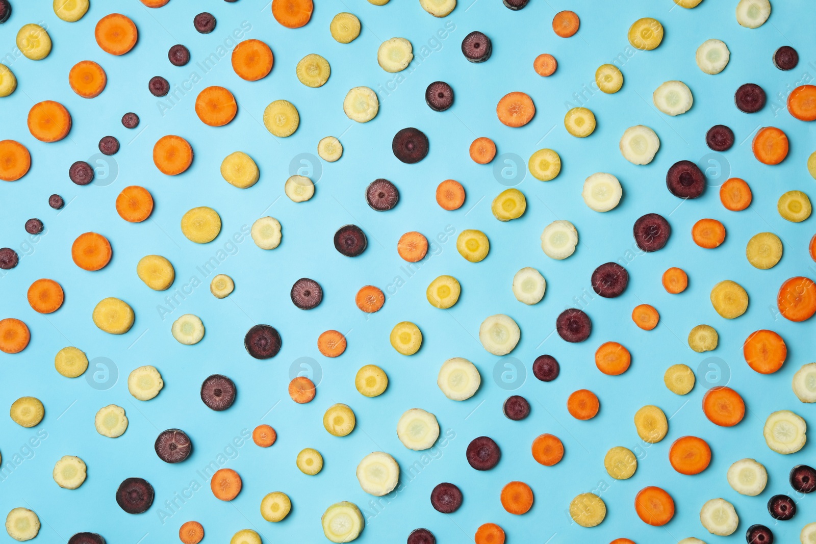 Photo of Slices of raw color carrots on light blue background, flat lay