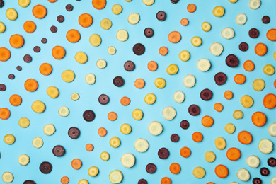 Slices of raw color carrots on light blue background, flat lay