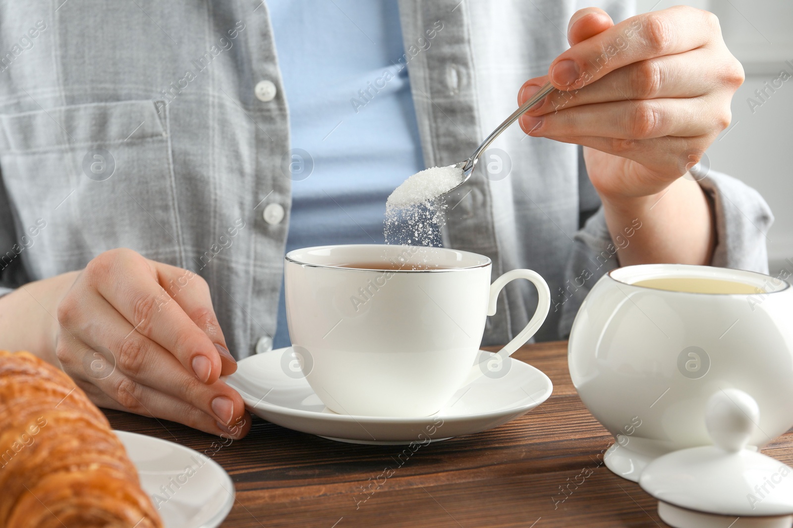 Photo of Woman adding sugar into cup of tea at wooden table, closeup