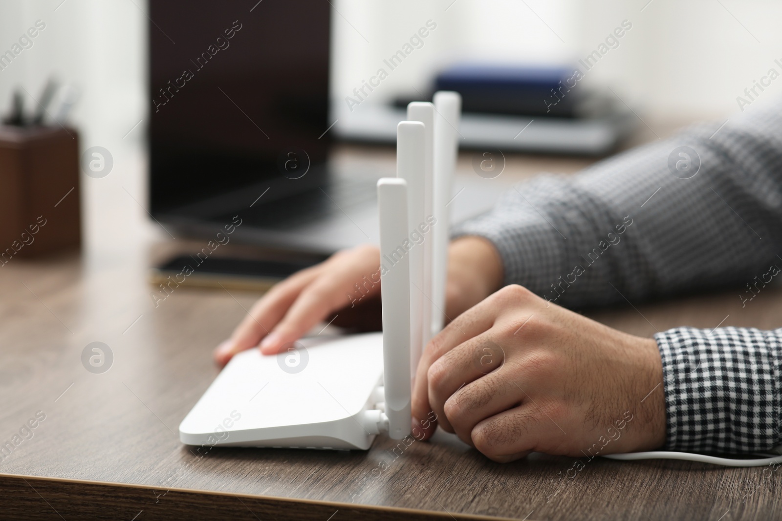 Photo of Man inserting cable into Wi-Fi router at wooden table indoors, closeup