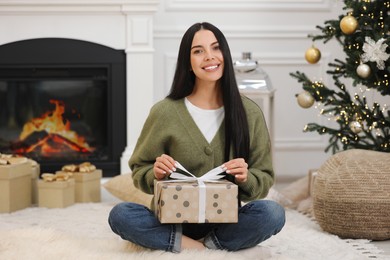 Photo of Smiling woman opening Christmas gift at home