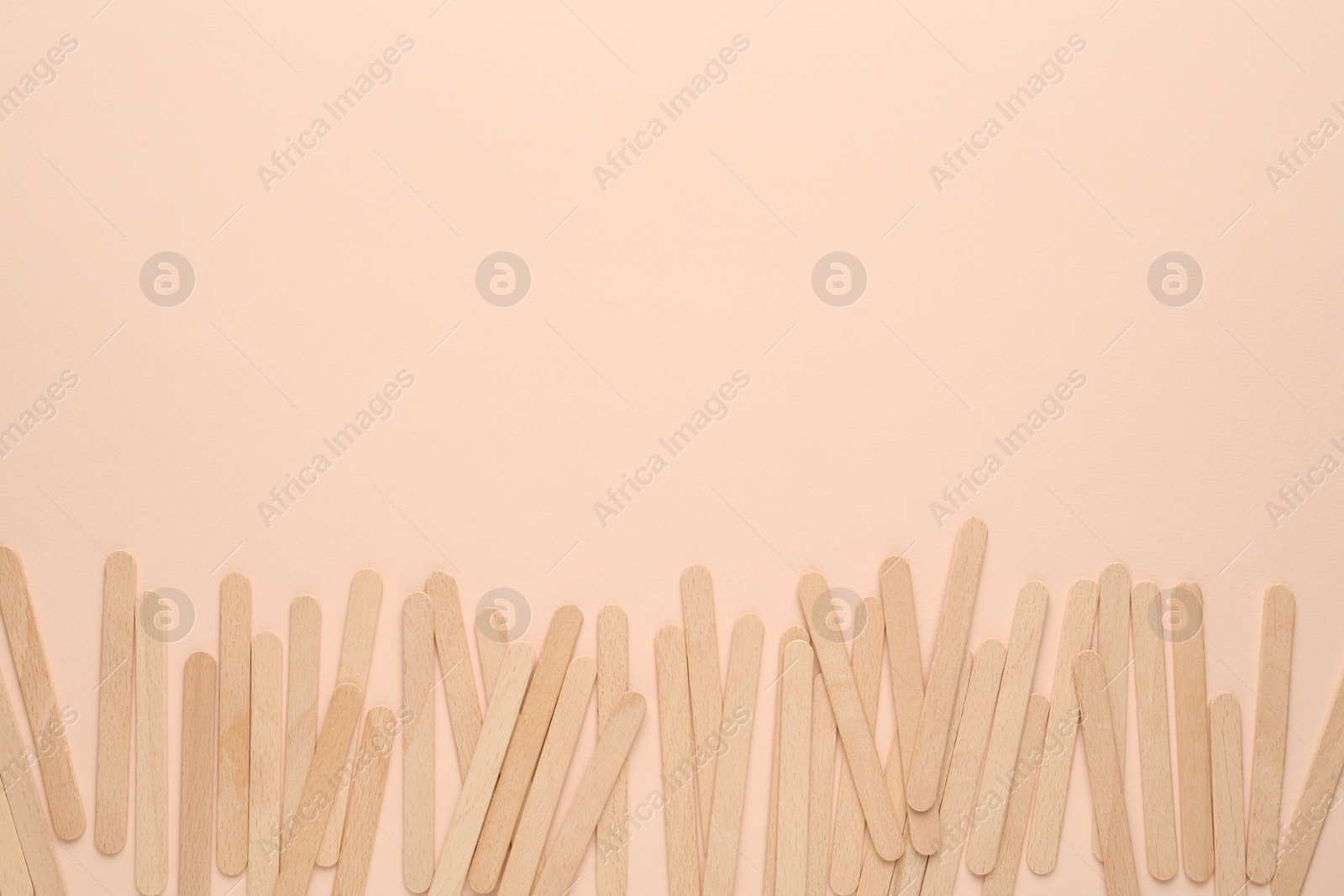 Photo of Wooden waxing spatulas on beige background, flat lay. Space for text