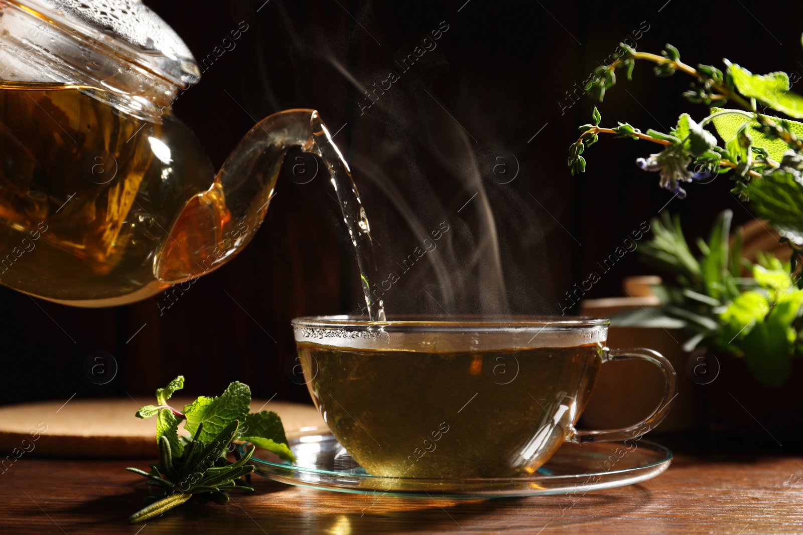 Photo of Pouring aromatic herbal tea into cup, mint and rosemary on wooden table