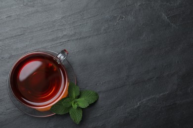 Photo of Cup of hot aromatic tea with mint on black table, flat lay. Space for text