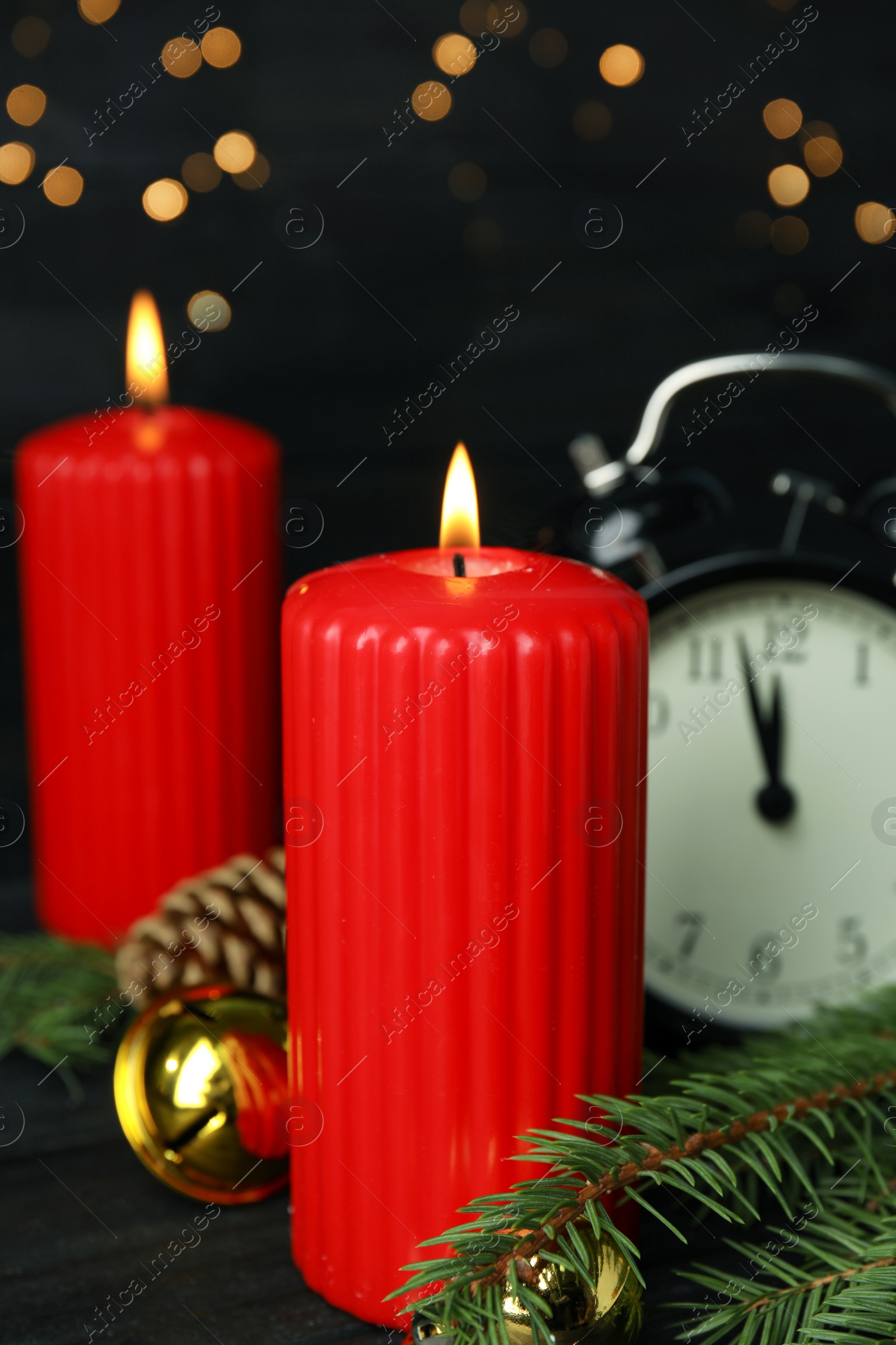 Photo of Burning candles, festive decor and alarm clock on wooden table against blurred Christmas lights