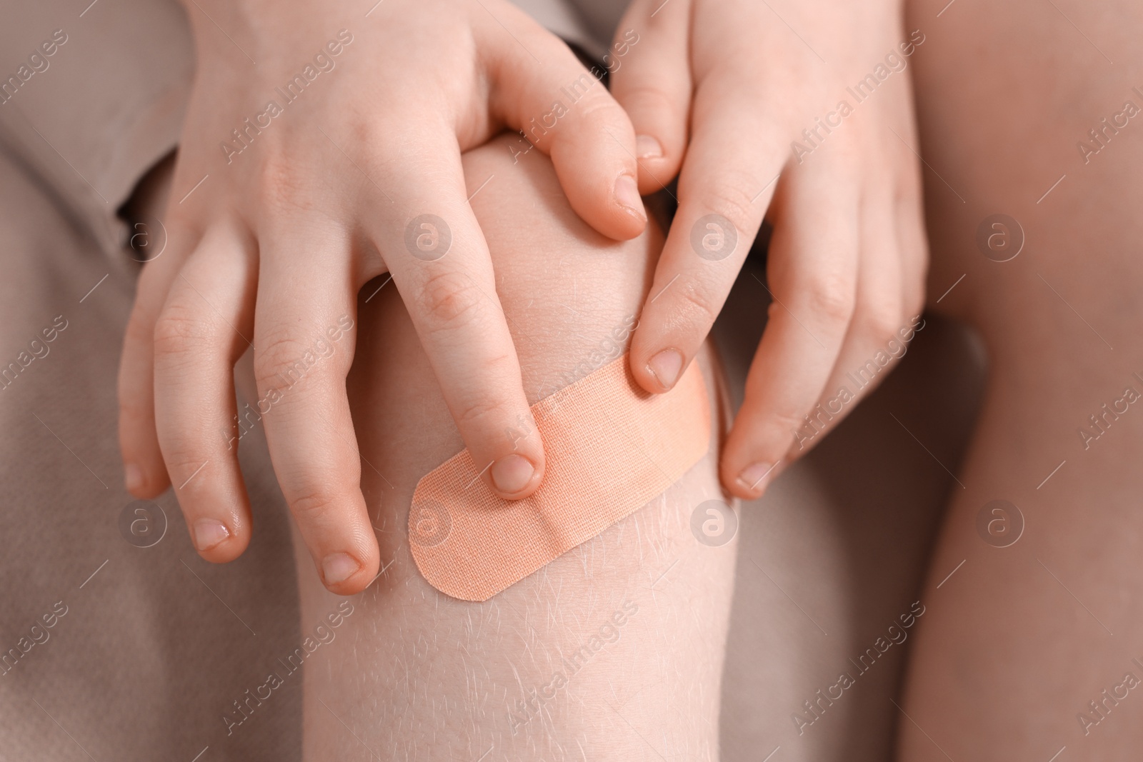 Photo of Little boy putting sticking plaster onto knee on sofa, closeup