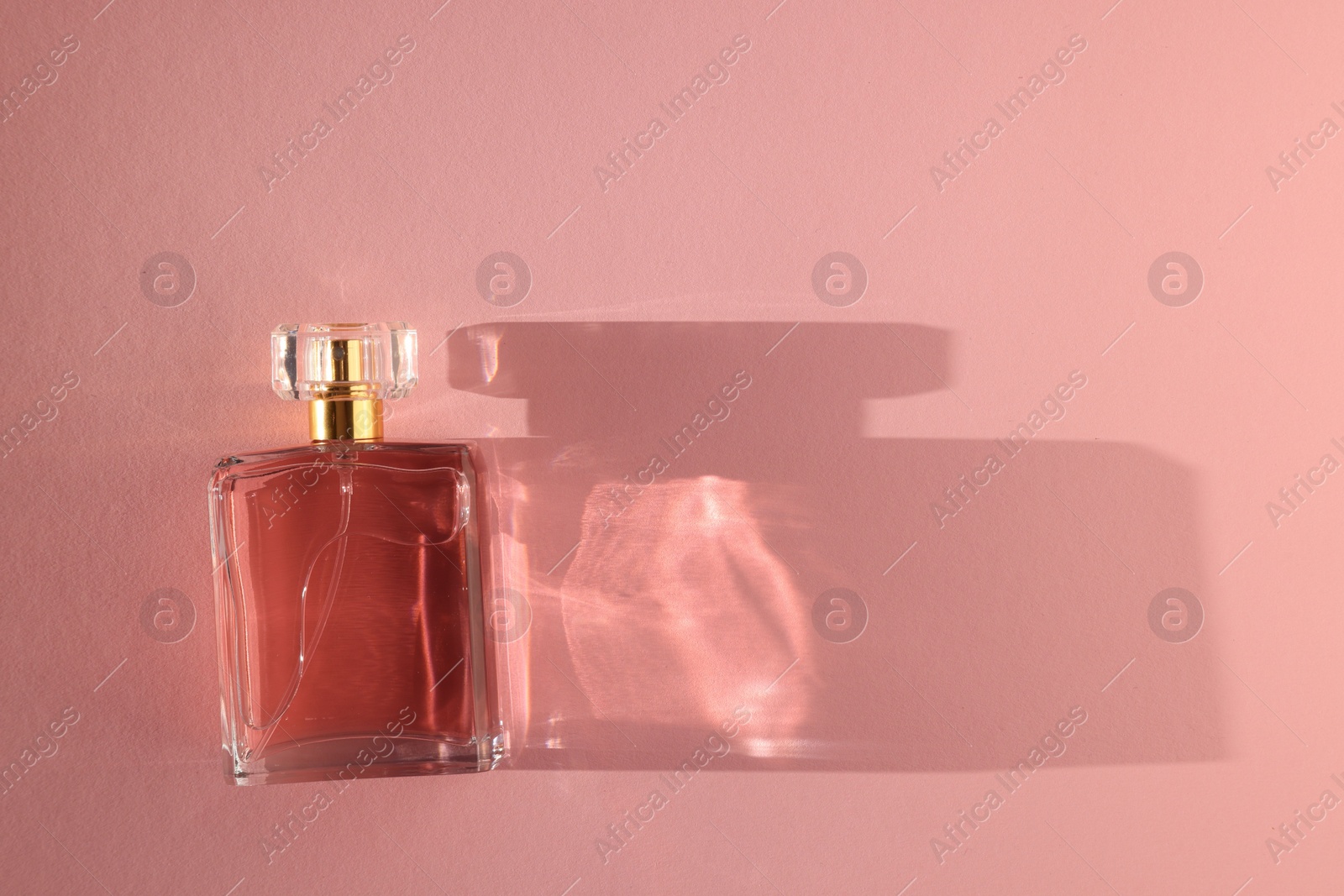 Photo of Luxury women's perfume. Sunlit glass bottle on pink background, top view. Space for text