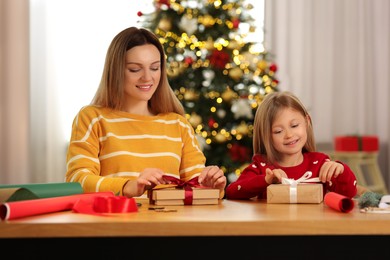 Christmas presents wrapping. Mother and her little daughter tying ribbon bows on gift boxes at home