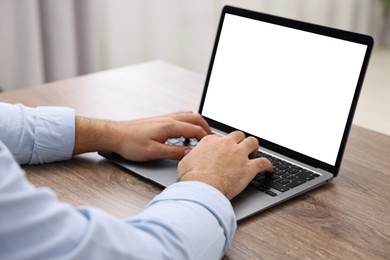 E-learning. Young man using laptop at wooden table indoors, closeup