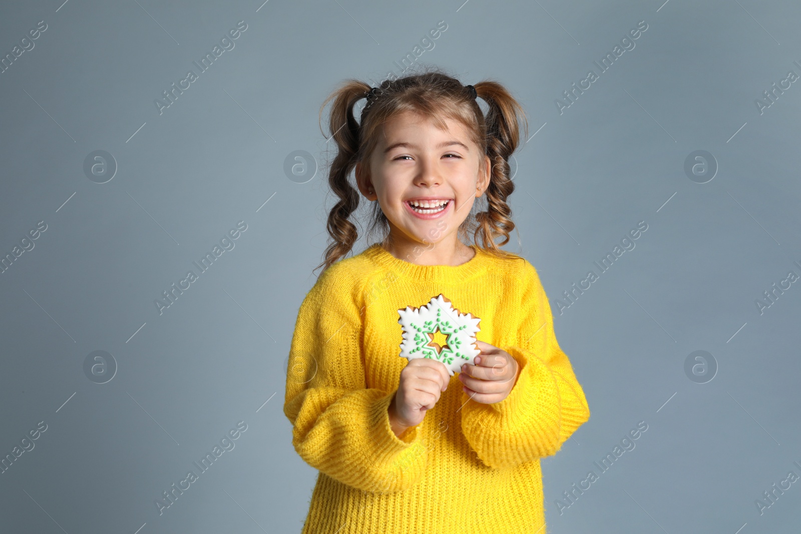 Photo of Cute little girl with Christmas gingerbread cookie on light grey background