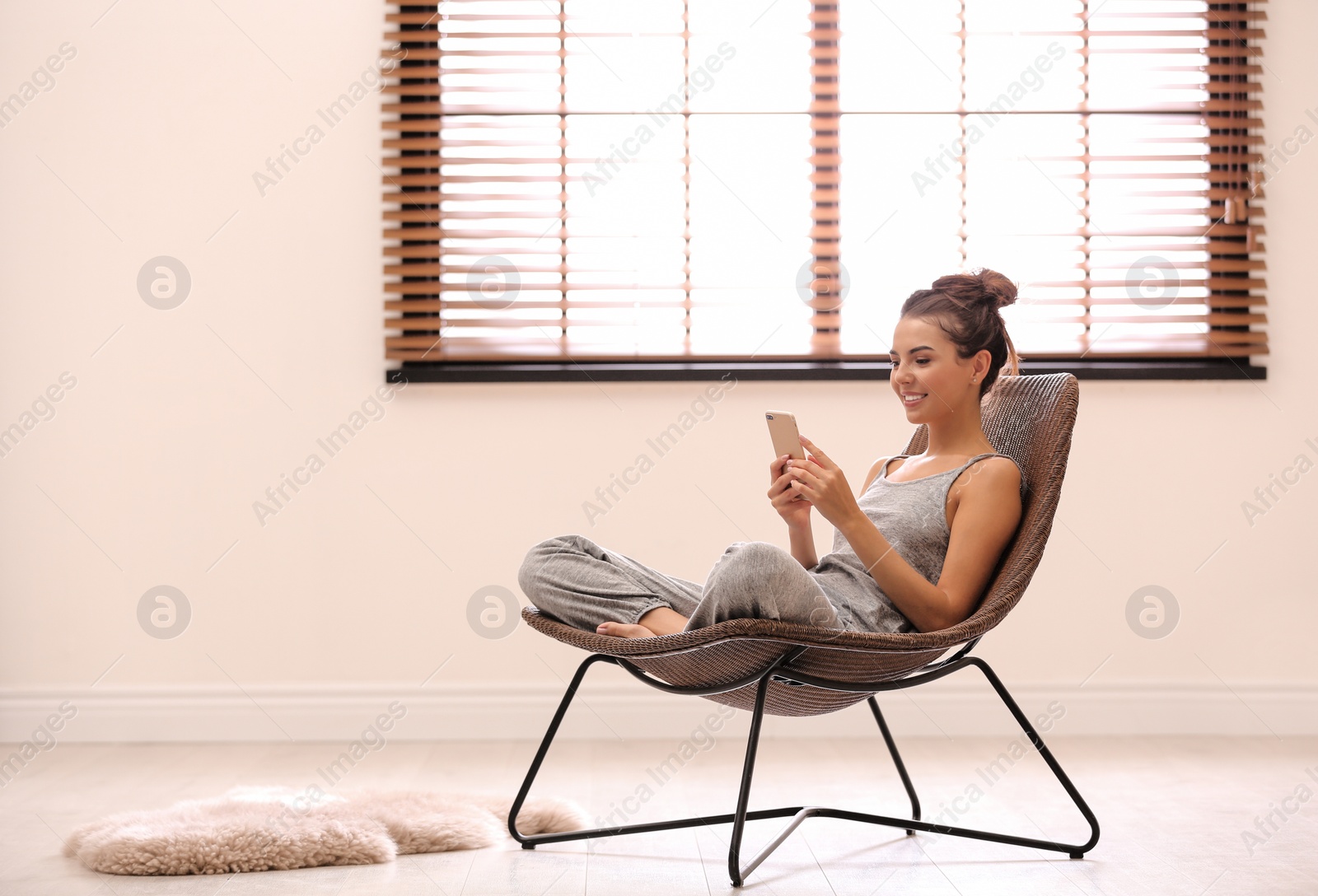 Photo of Young woman using smartphone near window with blinds at home. Space for text