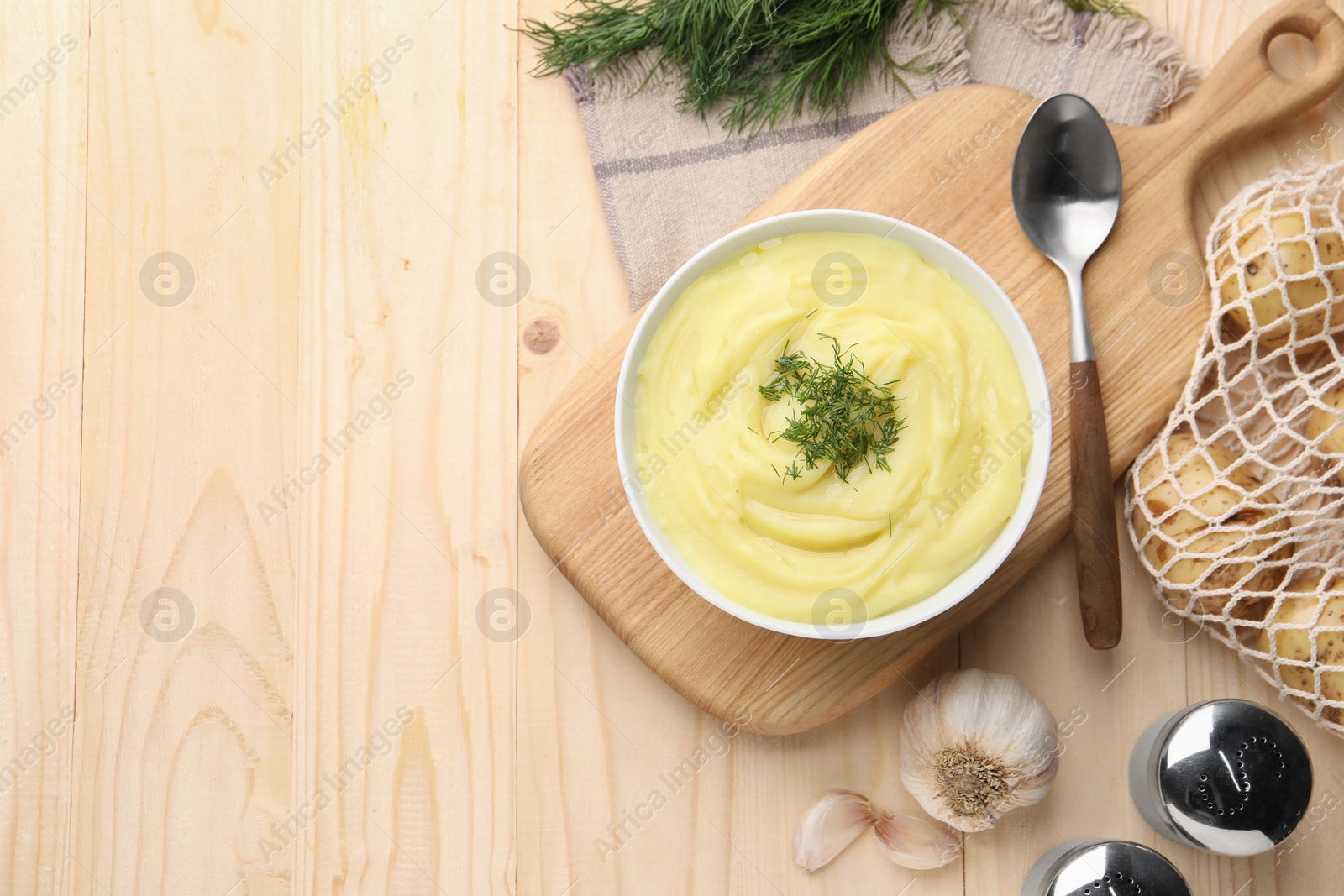 Photo of Bowl of tasty cream soup with dill, spoon and garlic on wooden table, flat lay. Space for text