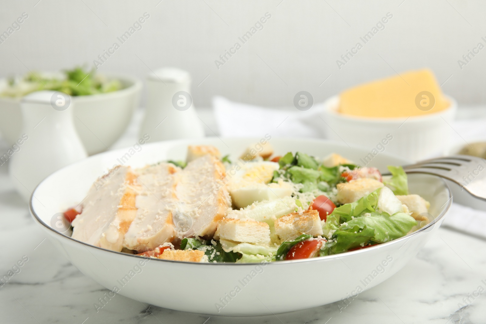 Photo of Delicious Caesar salad in bowl on white marble table