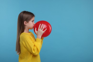 Cute girl inflating red balloon on light blue background, space for text