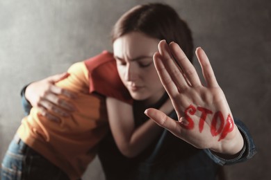 Photo of Scared little boy and mother with word Stop written on hand against light grey background, closeup. Domestic violence concept