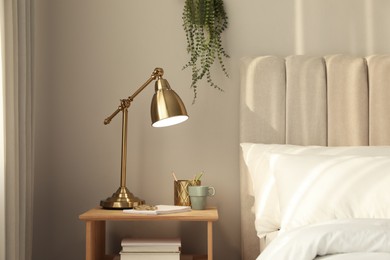 Photo of Stylish golden lamp and stationery on wooden nightstand in bedroom. Interior element