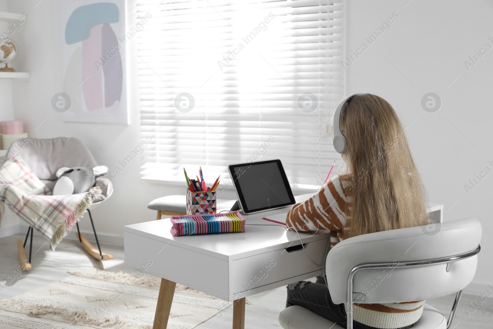 Photo of Cute little girl with modern tablet studying online at home, back view. E-learning