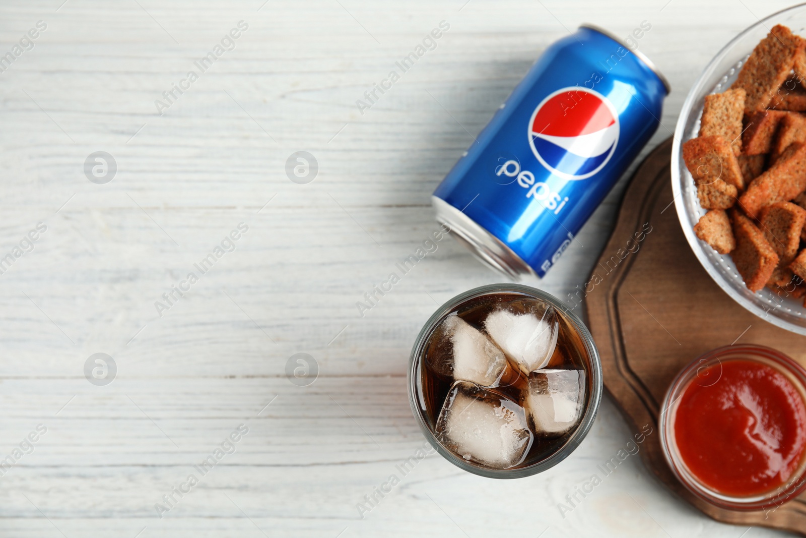 Photo of MYKOLAIV, UKRAINE - FEBRUARY 15, 2021: Glass of Pepsi, can and snack on white wooden table, flat lay. Space for text