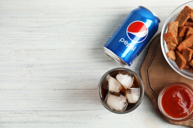 MYKOLAIV, UKRAINE - FEBRUARY 15, 2021: Glass of Pepsi, can and snack on white wooden table, flat lay. Space for text