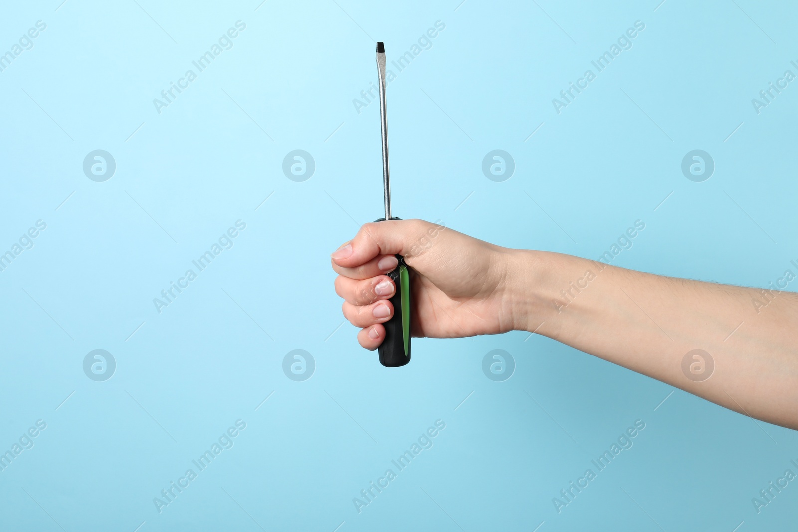 Photo of Woman holding screwdriver on light blue background, closeup