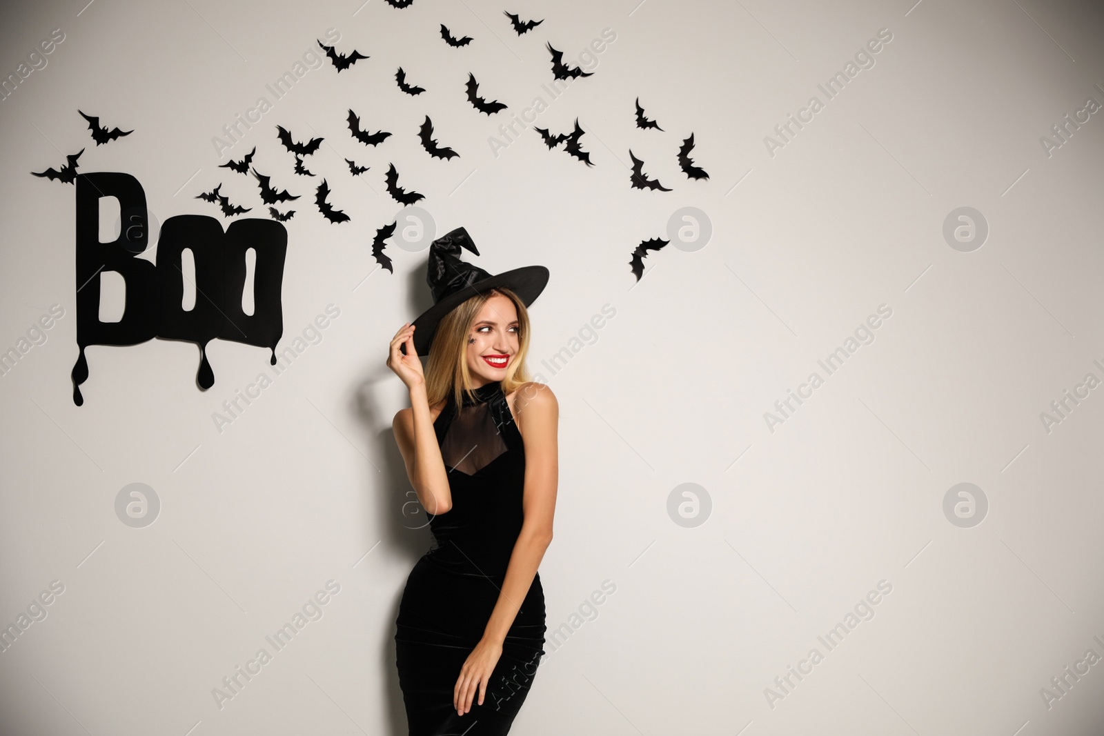 Photo of Woman in witch hat posing near white wall decorated for Halloween