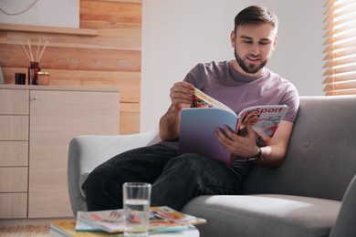 Photo of Young man reading sports magazine on sofa at home