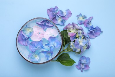 Photo of Spa composition. Aromatic water in bowl and flowers on light blue background, flat lay