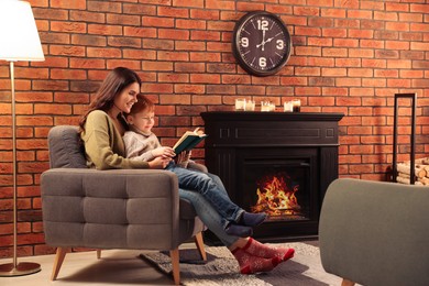 Photo of Happy mother and son reading book together near fireplace at home