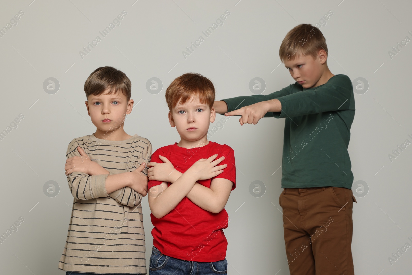 Photo of Boy pointing at upset kids on light grey background. Children's bullying