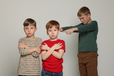 Boy pointing at upset kids on light grey background. Children's bullying