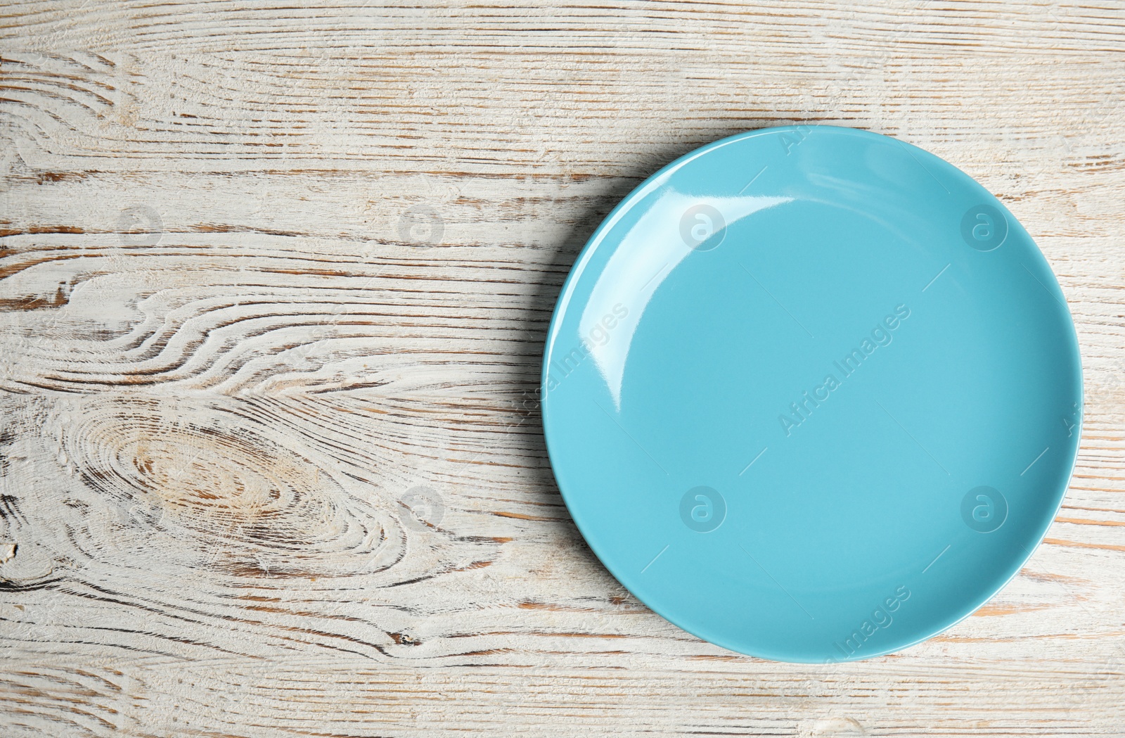 Photo of Empty light blue plate on white wooden table, top view. Space for text